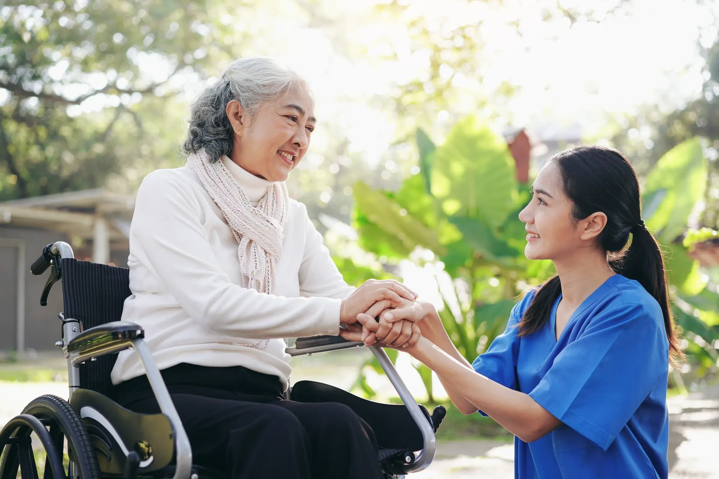 A caregiver holding the hands of an older woman seated in a wheelchair